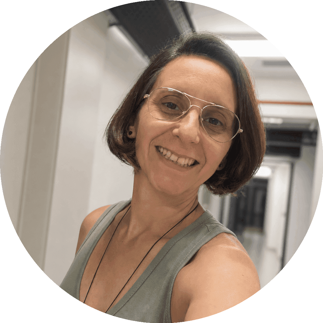 Retrato de Ju Panissa, mulher branca de cabelos castanhos curtos, usando óculos de armação fina e blusa verde, sorrindo.